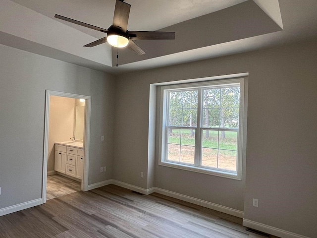 unfurnished bedroom with connected bathroom, light wood-style flooring, and baseboards