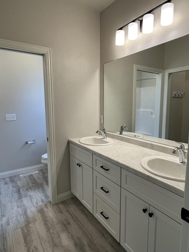 full bath with wood finished floors, toilet, double vanity, and a sink