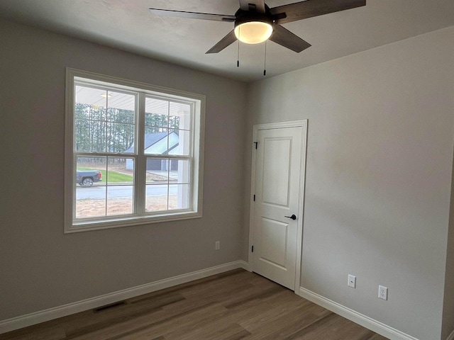 spare room with a ceiling fan, visible vents, wood finished floors, and baseboards
