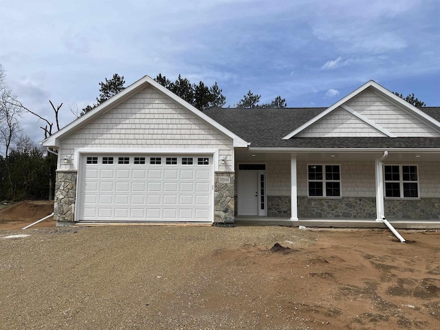 view of front of home featuring stone siding, a shingled roof, covered porch, and dirt driveway