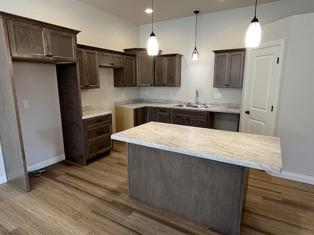 kitchen with dark brown cabinetry, wood finished floors, a kitchen island, a sink, and baseboards