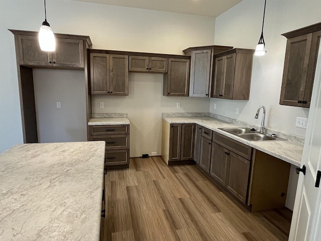 kitchen with a sink, light countertops, dark brown cabinets, wood finished floors, and hanging light fixtures