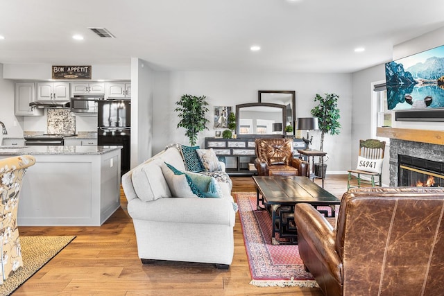living room featuring a high end fireplace, light wood finished floors, recessed lighting, and visible vents