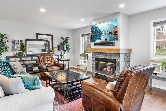 living room with recessed lighting, a stone fireplace, wood finished floors, and plenty of natural light
