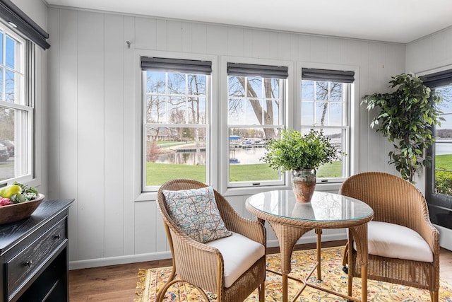 sitting room with a wealth of natural light, wood finished floors, a decorative wall, and a water view