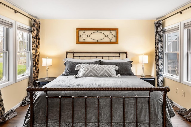 bedroom with baseboards, wood finished floors, and multiple windows
