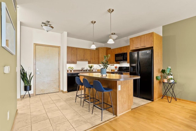 kitchen featuring a breakfast bar, a sink, a center island, decorative light fixtures, and black appliances