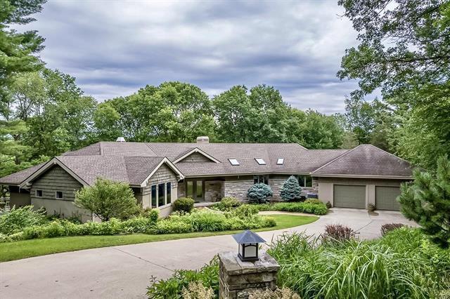 ranch-style house with a chimney, driveway, an attached garage, and stone siding