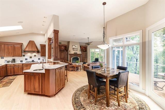kitchen with light wood-style flooring, brown cabinetry, ceiling fan, a sink, and a fireplace