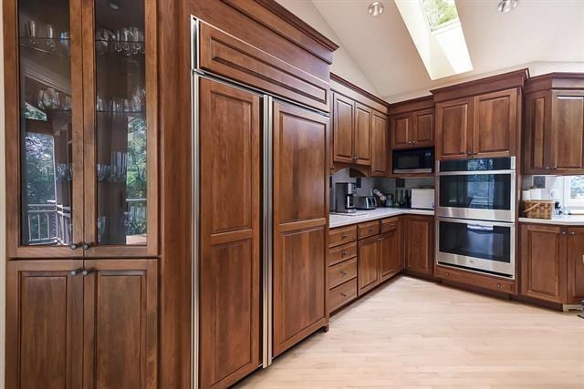 kitchen with built in appliances, lofted ceiling with skylight, light countertops, and light wood-type flooring