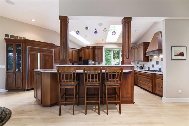 kitchen with wall chimney range hood, light countertops, vaulted ceiling, and decorative columns