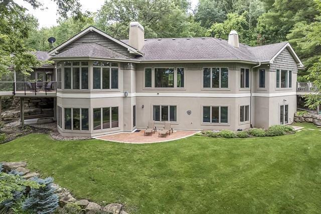 rear view of property with a patio, stucco siding, a chimney, and a lawn