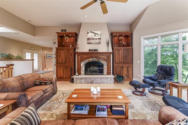living room with ceiling fan, a stone fireplace, visible vents, and wood finished floors