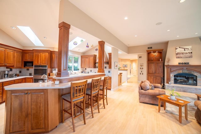 kitchen featuring brown cabinets, light countertops, open floor plan, built in microwave, and lofted ceiling with skylight