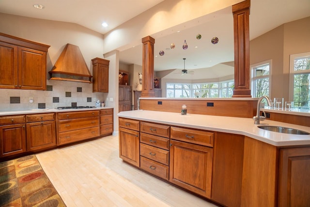kitchen with brown cabinets, decorative columns, custom range hood, and a sink