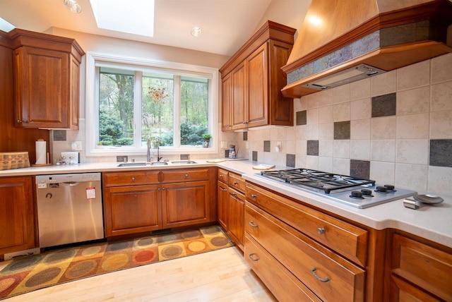 kitchen featuring a sink, tasteful backsplash, brown cabinets, custom exhaust hood, and appliances with stainless steel finishes