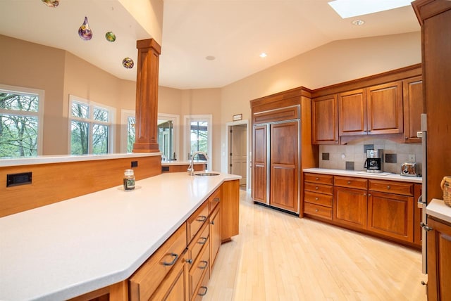 kitchen with a sink, brown cabinetry, paneled built in refrigerator, light wood finished floors, and light countertops