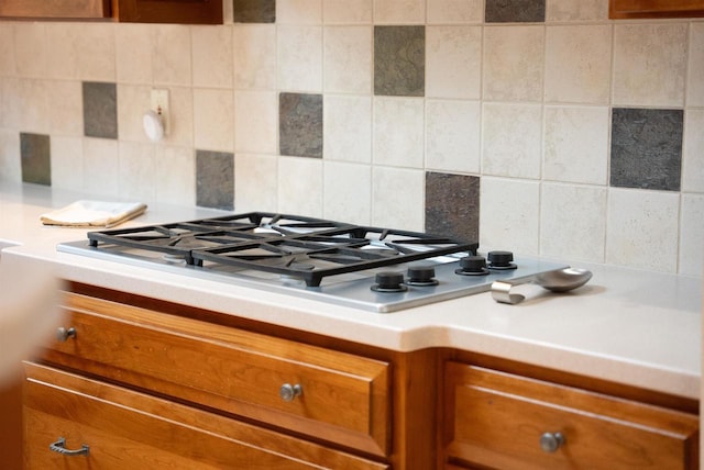 interior details with brown cabinetry, stainless steel gas stovetop, decorative backsplash, and light countertops
