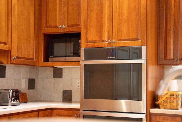 kitchen featuring brown cabinets, double oven, a toaster, decorative backsplash, and light countertops