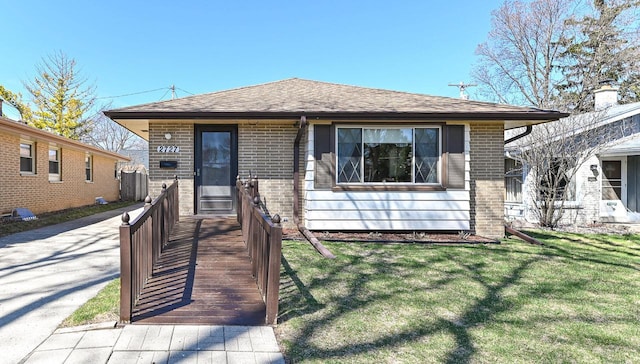 view of front of home featuring roof with shingles, a front lawn, and brick siding