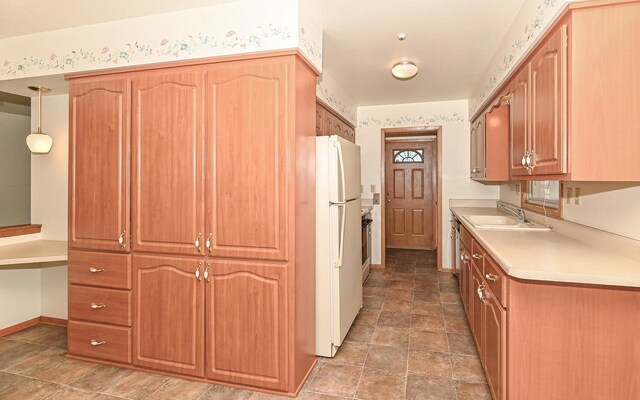 kitchen with a sink, stone finish flooring, light countertops, freestanding refrigerator, and baseboards