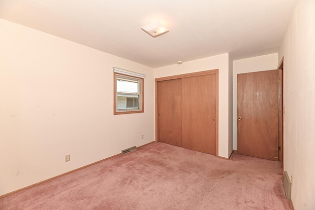 unfurnished bedroom featuring baseboards, visible vents, a closet, and light colored carpet