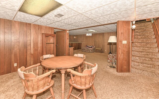 dining room with stairway, wooden walls, carpet floors, and a drop ceiling