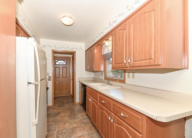 kitchen featuring a sink, dishwasher, light countertops, and freestanding refrigerator