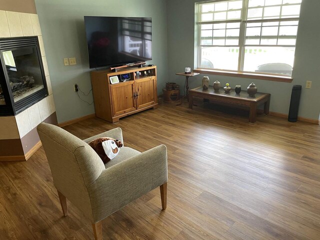 living area with wood finished floors, a tiled fireplace, and baseboards