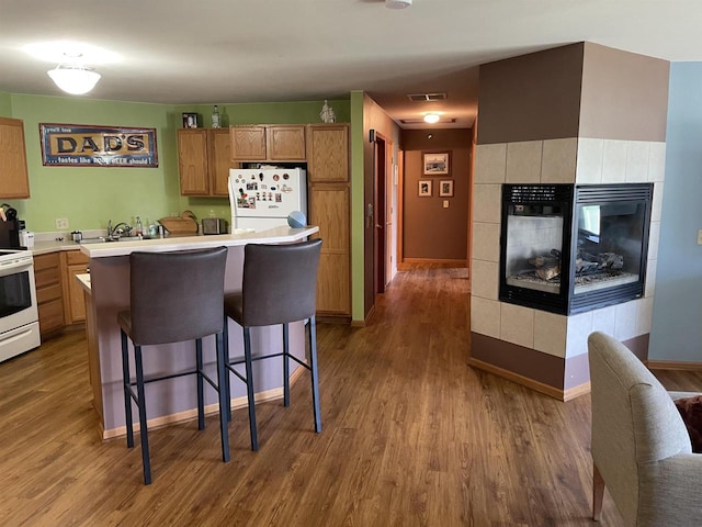 kitchen featuring a breakfast bar area, wood finished floors, white appliances, and light countertops