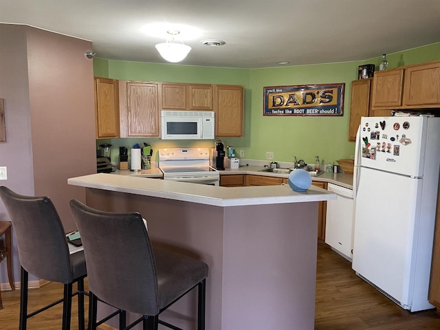 kitchen featuring a breakfast bar area, a sink, light countertops, dark wood finished floors, and white appliances