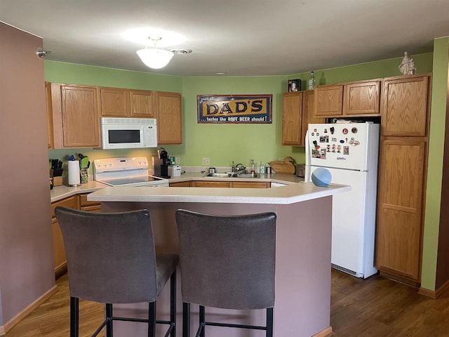 kitchen featuring white appliances, a breakfast bar area, a kitchen island, light countertops, and dark wood finished floors