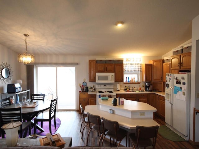 kitchen with dark wood finished floors, white appliances, a kitchen island, light countertops, and a sink