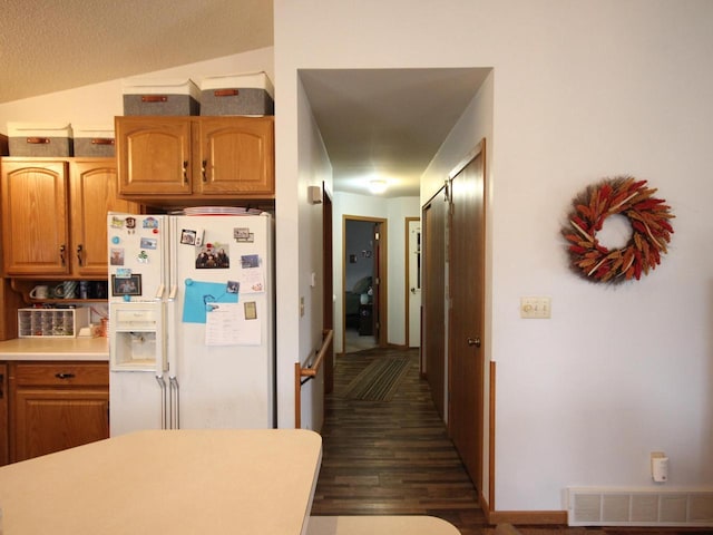 kitchen with white refrigerator with ice dispenser, visible vents, light countertops, dark wood finished floors, and brown cabinetry