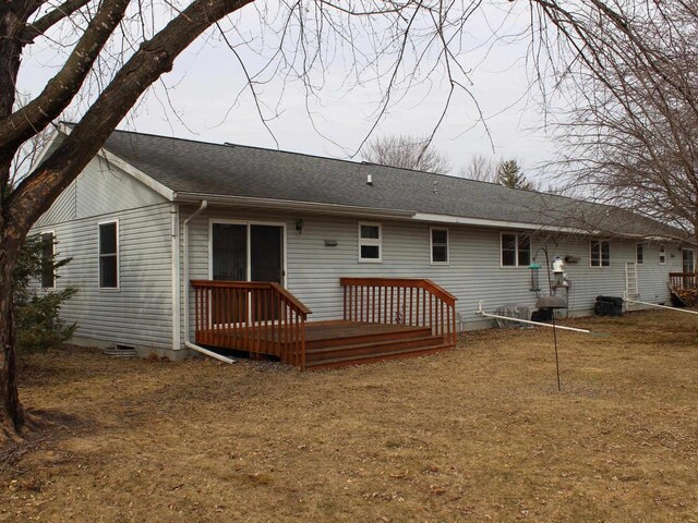 back of property with a lawn, a deck, and a shingled roof