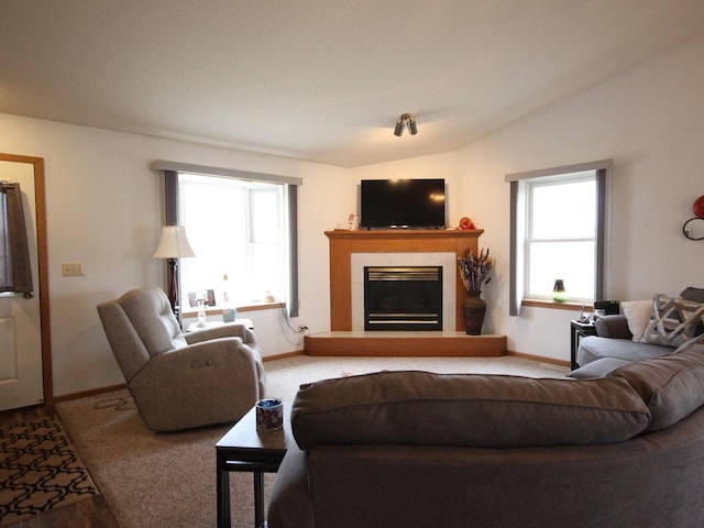 living room with a healthy amount of sunlight, a fireplace with raised hearth, vaulted ceiling, and baseboards