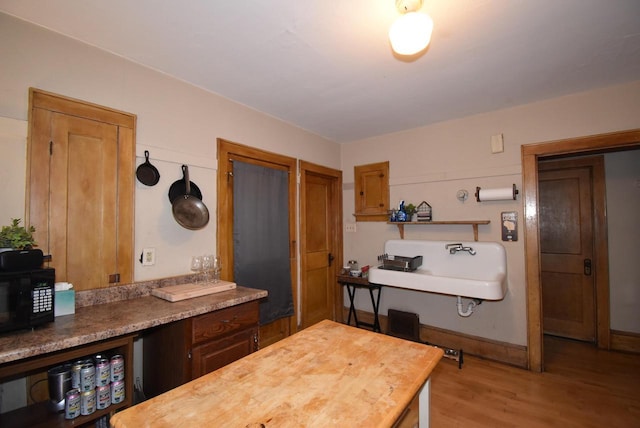 interior space with a sink, wood finished floors, black microwave, and wooden counters