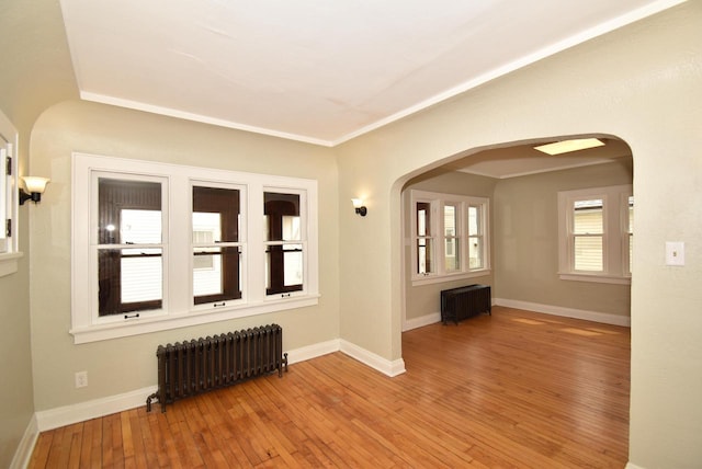 spare room featuring radiator heating unit, arched walkways, baseboards, and wood-type flooring
