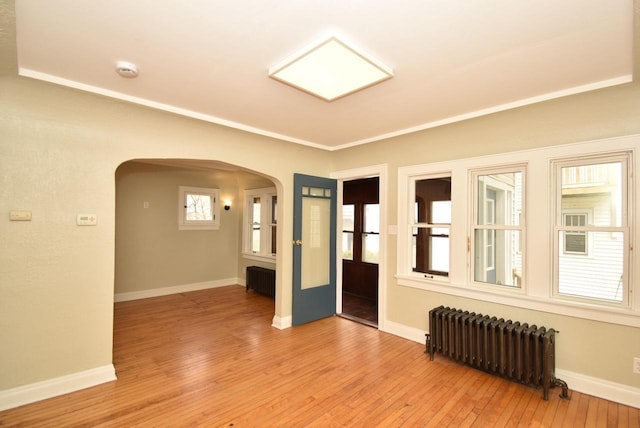 empty room featuring baseboards, arched walkways, light wood-style flooring, and radiator heating unit