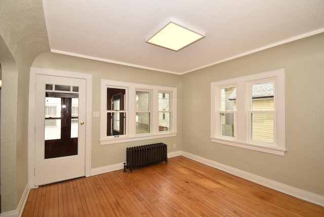 empty room featuring radiator, baseboards, light wood-type flooring, and arched walkways