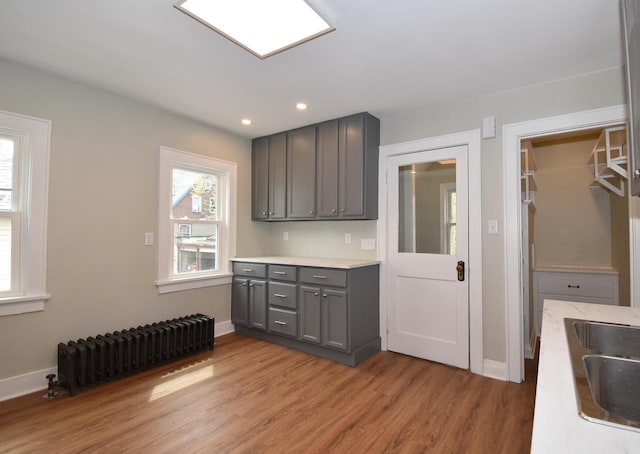 kitchen featuring gray cabinetry, light countertops, light wood finished floors, radiator, and recessed lighting