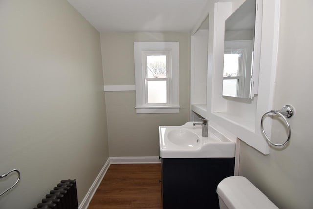 bathroom featuring wood finished floors, baseboards, vanity, toilet, and radiator heating unit