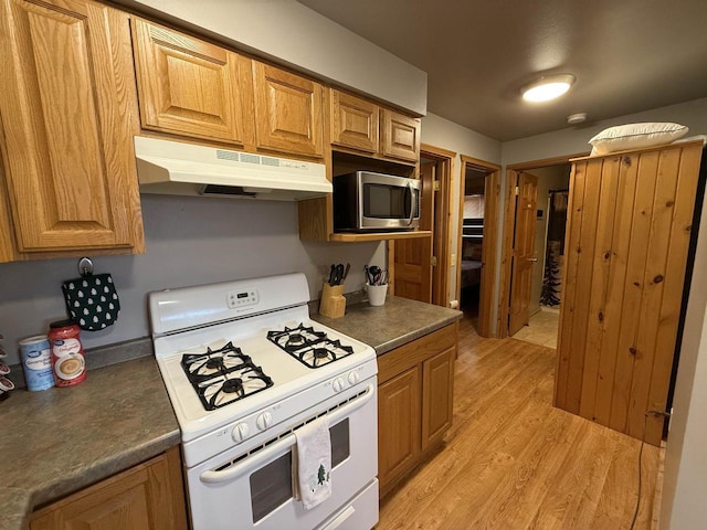 475 Overlook Ct, Warrens, WI 54666 - kitchen featuring stainless steel microwave, white gas range oven, under cabinet range hood, light wood-type flooring, and dark countertops