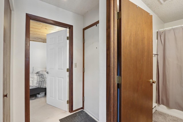 hallway with a textured ceiling, visible vents, and light colored carpet