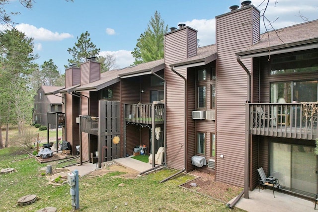 rear view of house with a chimney, a shingled roof, a balcony, and a yard