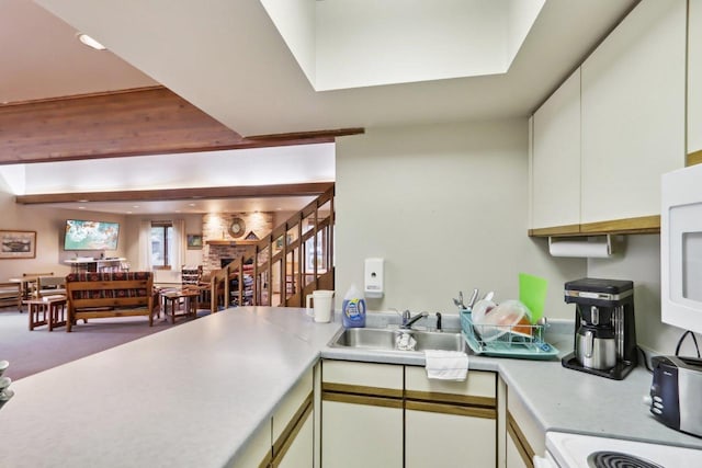 kitchen with a sink, range, white microwave, white cabinetry, and light countertops