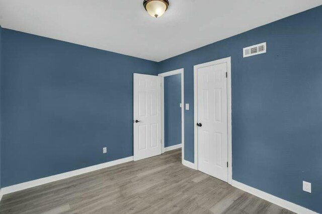 unfurnished bedroom with baseboards, visible vents, and wood finished floors