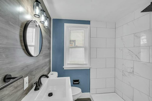 full bath with toilet, a sink, tiled shower, and baseboards