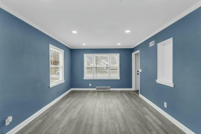 unfurnished room with visible vents, wood finished floors, ornamental molding, and baseboards