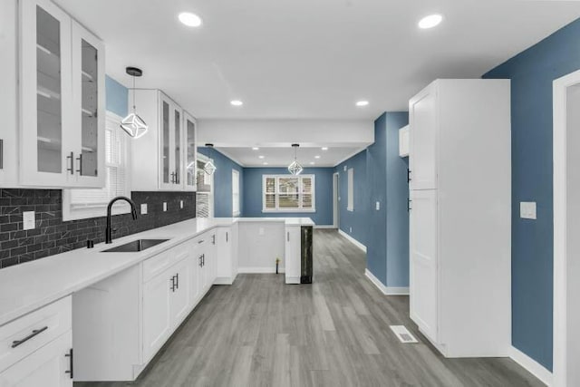 kitchen with a sink, light wood-type flooring, backsplash, a peninsula, and white cabinets